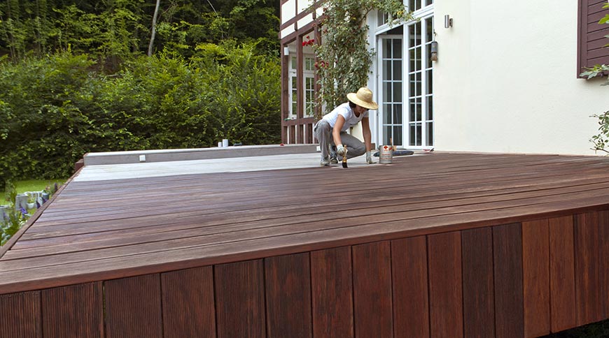 Frau streicht Terrasse mit Terrassenholzöl